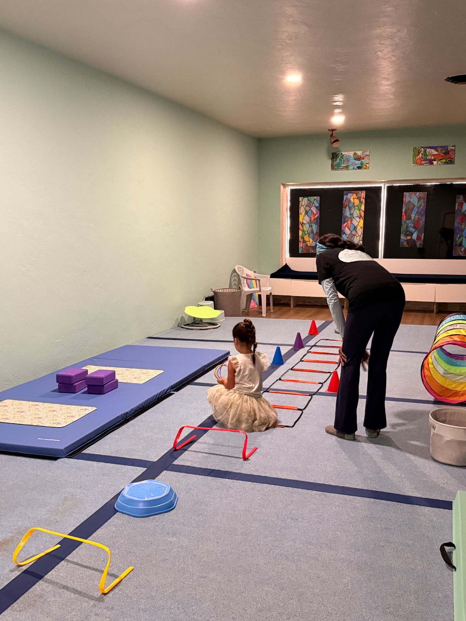 Child navigating an indoor obstacle course with instructor support